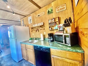 A kitchen with wooden cabinets, a refrigerator, a dishwasher, a microwave, and a coffee maker. There are signs on the wall, including one that says 'DON'T FEED THE BEARS.'
