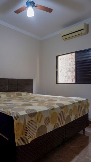 Ein Schlafzimmer mit Bett, Deckenventilator, Klimaanlage und Fenster mit Blick auf eine Ziegelwand.