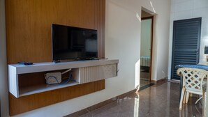 Een moderne woonkamer met een flatscreen televisie bevestigd aan een houten paneel, een witte kast eronder, en een eethoek met een tafel en stoelen.