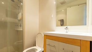 Ein Badezimmer mit Toilette, Duschkabine aus Glas, Waschbecken und Spiegel.