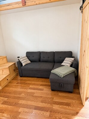 A room with a dark grey sectional sofa, a wooden chest of drawers, and a wooden floor.