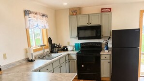 Una cocina con armarios de madera, microondas, estufa, refrigerador y ventana con vista.