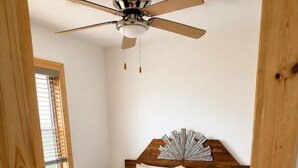 Un dormitorio con cama, cabecero de madera, ventilador de techo y ventana con persianas.