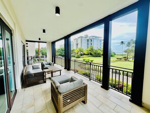 Ein geräumiger Balkon mit Sofa und Tisch, große Fenster mit Blick auf einen gepflegten Garten und Gebäude.