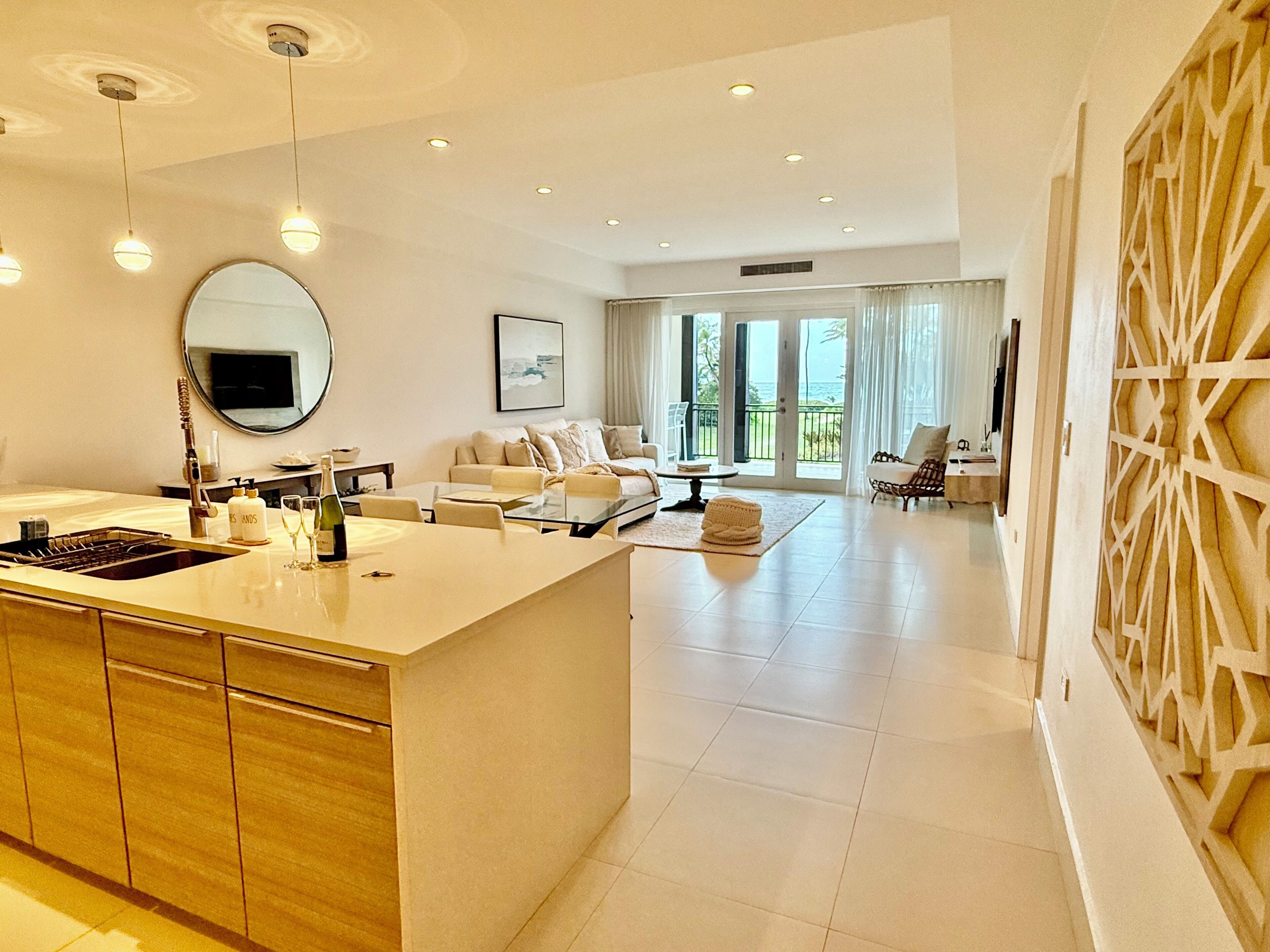 A modern kitchen with a central island, a dining area with a glass table, and a living room with a sofa and a TV.