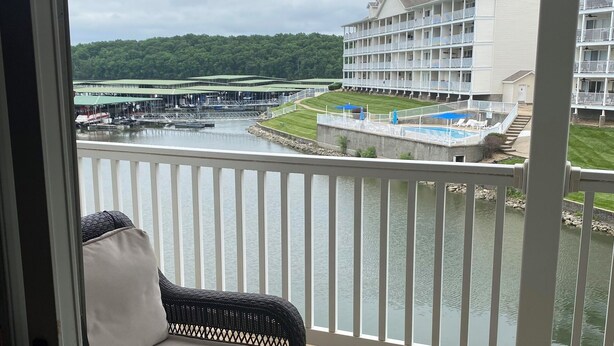 A balcony with a wicker sofa, a view of a lake, a building with multiple balconies, and a dock with boats. - Charming 2 bedroom lakefront condo with access to 3 outdoor pools in Osage Beach (Osage Beach)