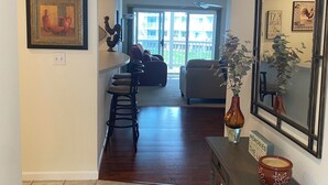 A hallway with a tiled floor, a framed painting, a mirror, a console table with a vase, and a door leading to a living room with a sofa and a dining area. - Charming 2 bedroom lakefront condo with access to 3 outdoor pools in Osage Beach (Osage Beach)