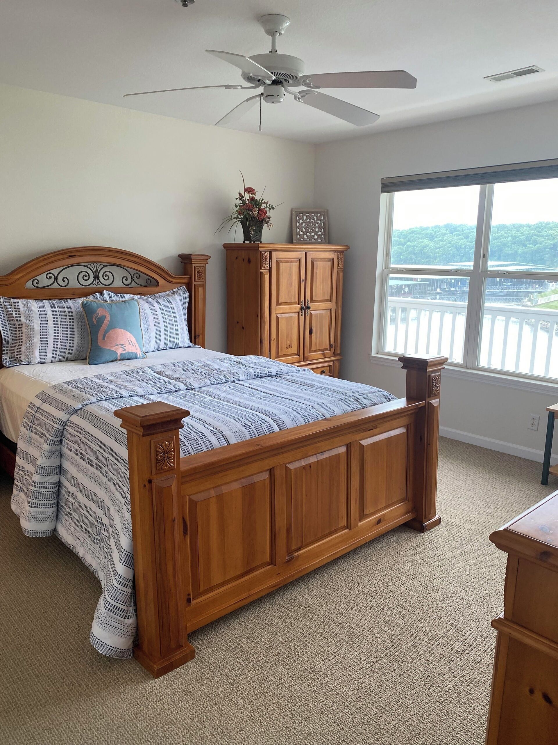 Une chambre à coucher avec un lit en bois, un ventilateur de plafond, une fenêtre donnant sur un beau paysage et une armoire en bois.