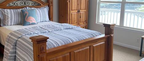 A bedroom with a wooden bed, a ceiling fan, a window with a view, and a wooden cabinet.
