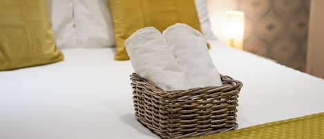 Una cama con ropa blanca, una cesta de mimbre con toallas y decoración mural estampada.