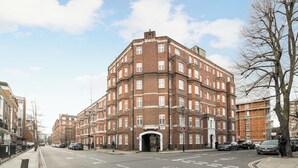 A multi-story brick building with a central entrance, adjacent to a street with parked cars. - Central London Gem | Sleeps 8 | Hyde Park | London (London)