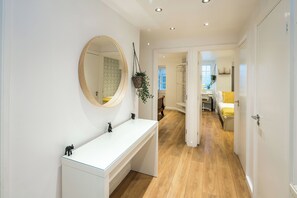 Un baño moderno con tocador blanco, un espejo redondo y una planta colgante.