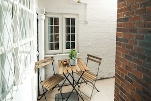 En hyggelig terrasse med et træbord og stole, en potteplante og et hvidt vindue med udsigt.