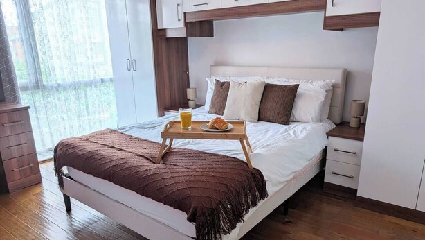 Een moderne slaapkamer met een bed, nachtkastjes, een houten vloer en een raam met gordijnen.