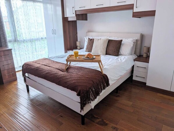 A modern bedroom with a bed, bedside tables, a wooden floor, and a window with curtains.