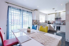 A modern kitchen with a dining area, a large window with blue curtains, and a kitchen island. - The Eastern Hive - 3x Parking | Co-op Live&Etihad (Greater Manchester)