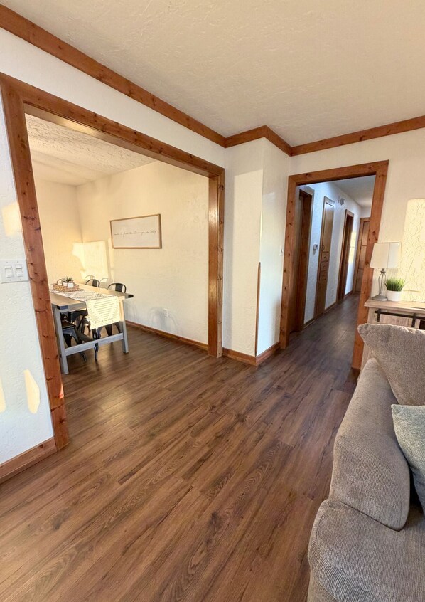 A hallway with wooden flooring, a dining area with a table and chairs, and a sofa.
