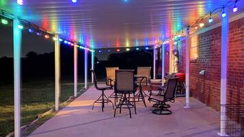 Un patio couvert agrémenté de guirlandes lumineuses, de mobilier d’extérieur et d’un mur en briques.
