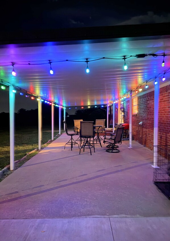 A covered patio area with string lights, outdoor furniture, and a brick wall.
