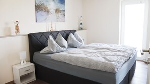 A bedroom with a bed, nightstand, and a painting on the wall. - Ullrichshof Vacation Rental in Upper Lusatia – Sauna, BBQ Area & Panoramic View (Großdubrau)