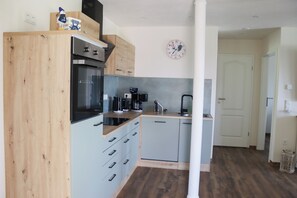 A modern kitchen with wooden cabinets, a built-in oven, a coffee maker, and a clock on the wall. - Ullrichshof Vacation Rental in Upper Lusatia – Sauna, BBQ Area & Panoramic View (Großdubrau)