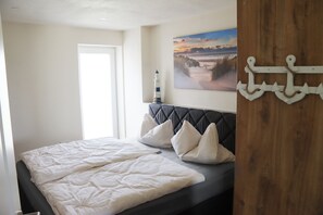 A bedroom with a bed, pillows, a painting, and a wooden wall. - Ullrichshof Vacation Rental in Upper Lusatia – Sauna, BBQ Area & Panoramic View (Großdubrau)
