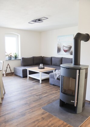 Een moderne woonkamer met een grijze bank, een witte salontafel en een zwarte houtkachel.