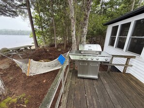 Un hamac, un barbecue et une terrasse en bois au bord d’un lac.