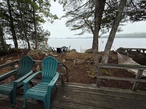 A wooden deck with Adirondack chairs and a hammock overlooking a lake.