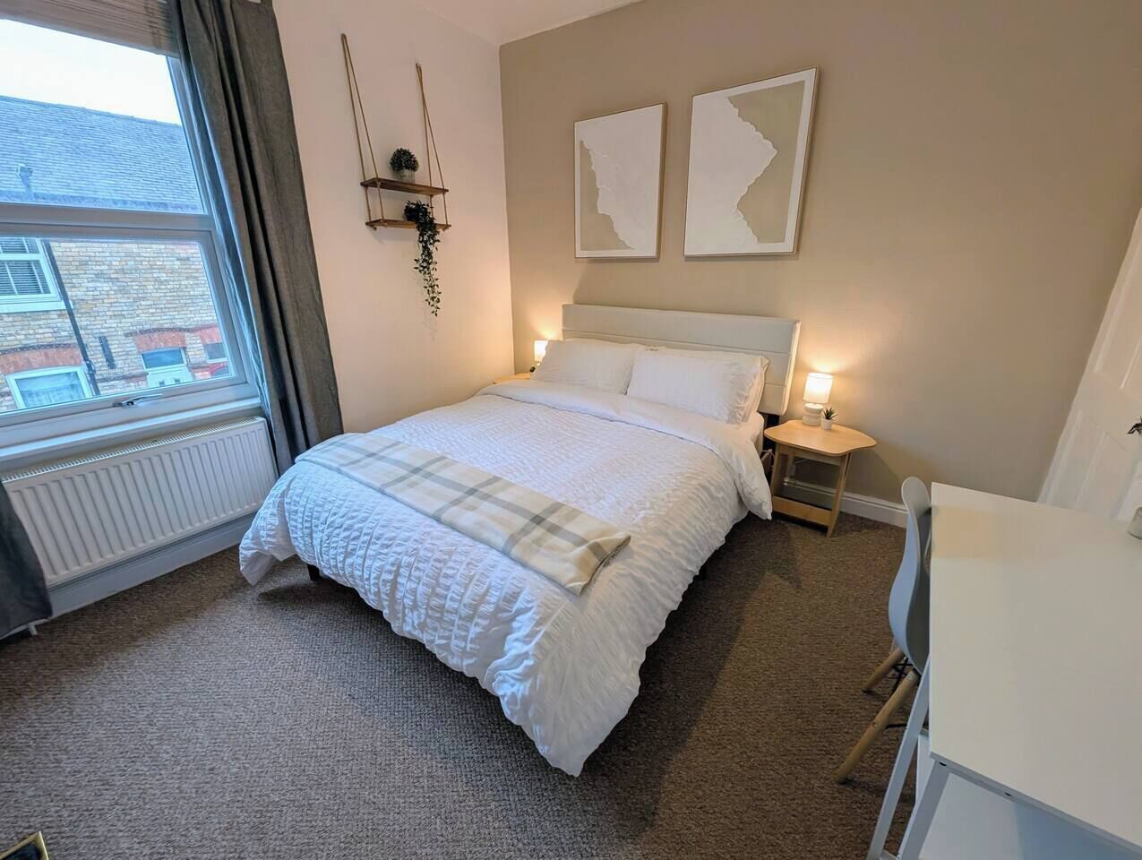 A bedroom with a bed, bedside tables, a desk, and a window.