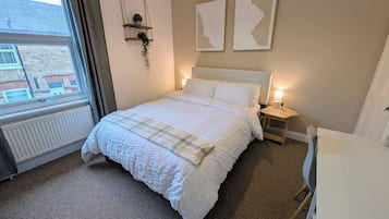 A bedroom with a bed, bedside tables, a desk, and a window.