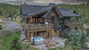 Une maison moderne à deux étages, dotée d’un jacuzzi, d’un espace salon extérieur et d’une terrasse offrant une vue sur une zone boisée.