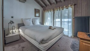 Een slaapkamer met een groot bed, een nachtkastje met een lamp, een lijst met een foto aan de muur en een raam met gordijnen.