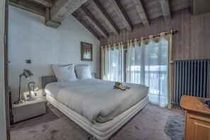 Ein Schlafzimmer mit einem großen Bett, einem Nachttisch mit Lampe, einem gerahmten Bild an der Wand und einem Fenster mit Vorhängen.