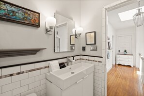 A bathroom with a white sink, vanity, and a mirror. There is a framed picture on the wall and a chandelier. - Hill East, Barney Circle 2-BR, Walk to METRO Stop (Washington)