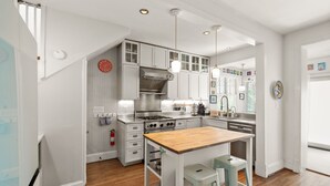 Une cuisine moderne avec des meubles blancs, un îlot central en bois et des luminaires suspendus.