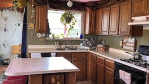 A kitchen with wooden cabinets, a central island, a stove, and a window with a view. - Cozy room, Quiet home (Arcata)