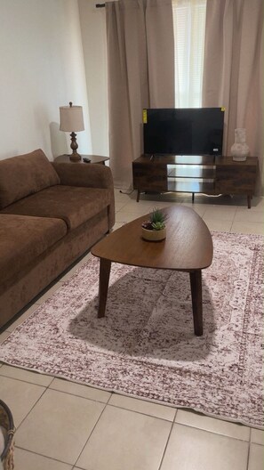 A living room with a sofa, a coffee table with a plant, a TV on a wooden stand, and a lamp. - Houston 1-bedroom unit 42 condo with AC easy access to FWY (Houston)