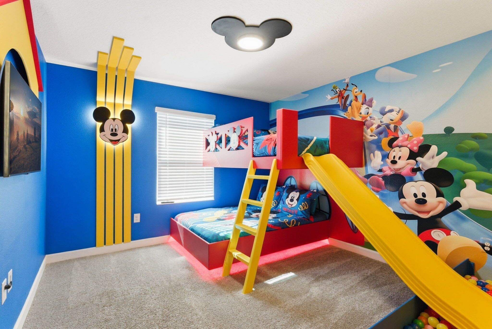 A child's bedroom with a bunk bed, a ladder, a slide, and Mickey Mouse-themed decorations.
