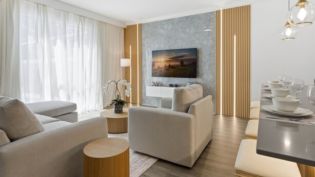 Ein modernes Wohnzimmer mit Sofa, Sesseln, Couchtisch und Essbereich mit Tisch für vier Personen.