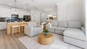 Ein modernes Wohnzimmer mit einer Couch, einem Couchtisch und einer Küchenzeile im Hintergrund.
