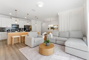 Ein modernes Wohnzimmer mit einer Couch, einem Couchtisch und einer Küchenzeile im Hintergrund.
