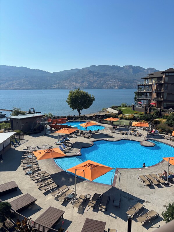 A resort with a large pool, lounge chairs, and a view of mountains.