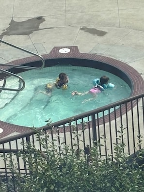 A small outdoor hot tub with metal railings and a brick border.