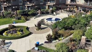 Un edificio residencial de varios pisos con balcones, un patio central con una fuente circular y abundante vegetación circundante.