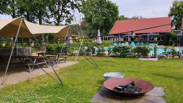 Et picnicområde med et bord, stole, grill og en pool i baggrunden.