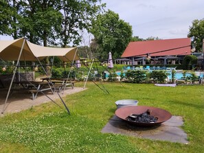 Un espace pique-nique équipé d’une table et de chaises, d’un barbecue et, au fond, d’une piscine.