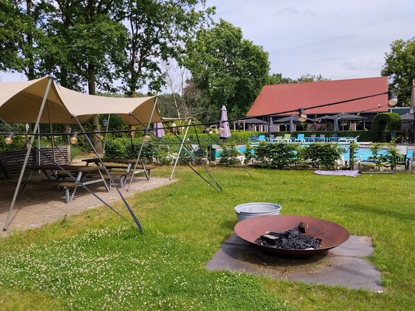 Un espace pique-nique équipé d’une table et de chaises, d’un barbecue et, au fond, d’une piscine.