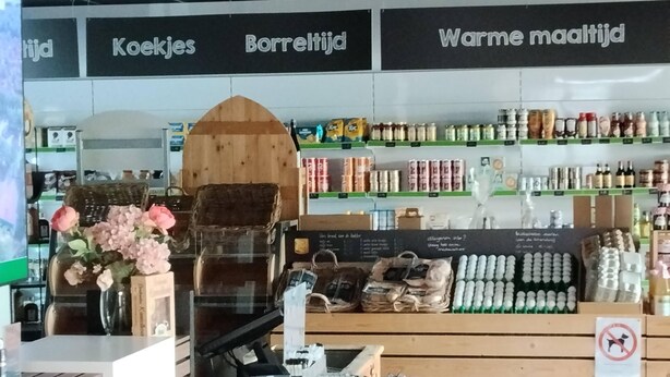 L’intérieur d’un magasin, avec des étagères remplies de produits, un présentoir en bois et une enseigne portant un texte dans une langue étrangère.