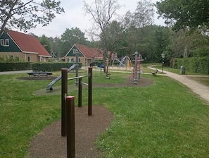 A playground with swings, a slide, and climbing structures surrounded by grass and trees.